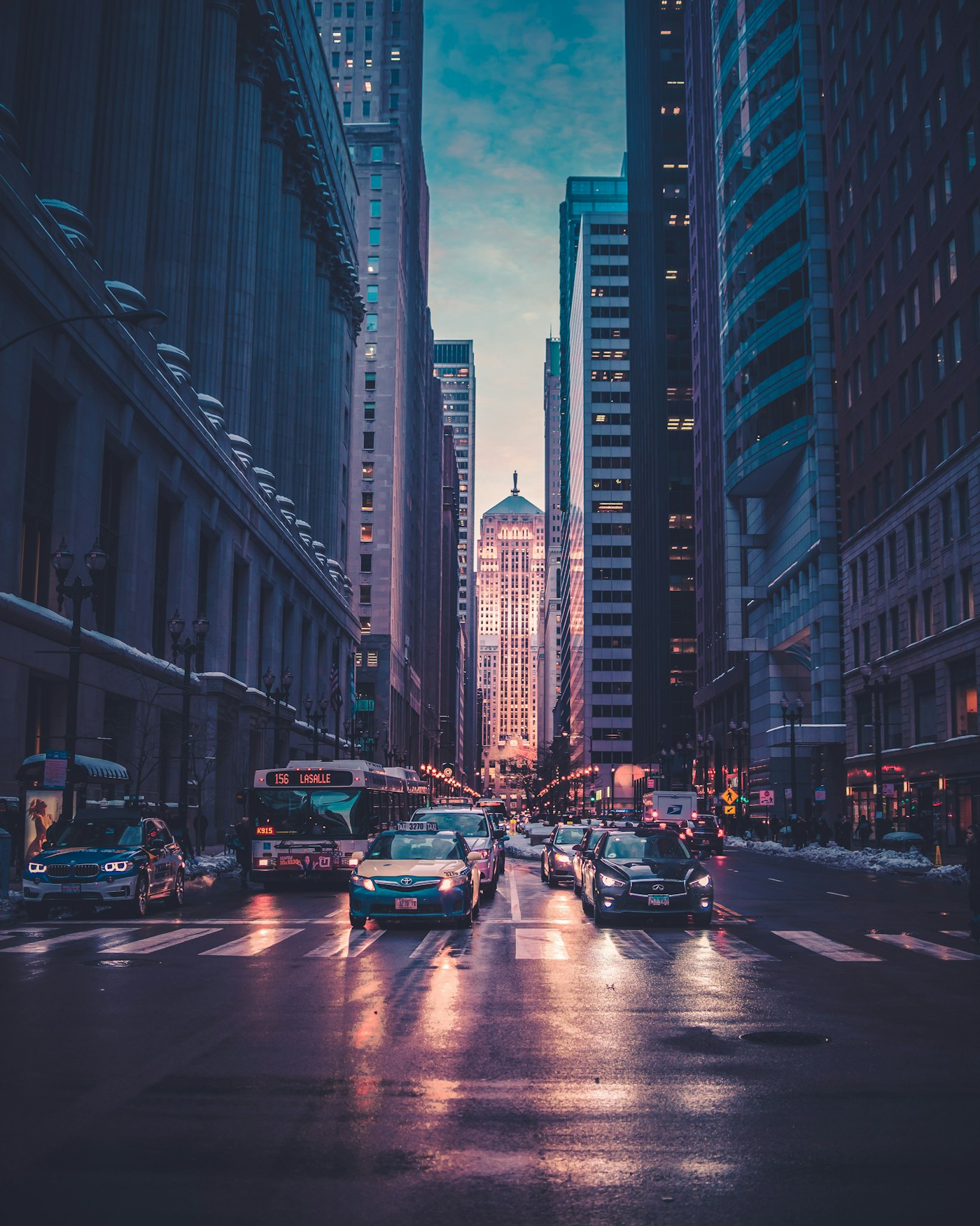 Illustrative night view of a wet city street, lit windows and passing traffic.